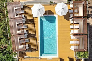 Ein Poolbereich auf dem Dach mit mehreren Liegestühlen und Sonnenschirmen, umgeben von einem Holzboden.