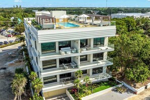 A multi-story hotel with a rooftop pool, outdoor seating, and lush landscaping. - The Sands 5: 7Mile Beach Condo w/Rooftop Pool & Beach Deck (West Bay)