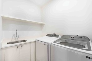 A laundry area with a sink, two washing machines, and a countertop. - The Sands 5: 7Mile Beach Condo w/Rooftop Pool & Beach Deck (West Bay)