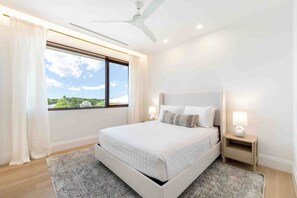 Ein modernes Schlafzimmer mit einem großen Bett, einem Nachttisch mit Lampe und Blick auf Grün durch das Fenster.