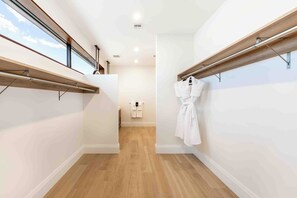 A narrow hallway with wooden flooring, white walls, and a wooden beam running along the ceiling. A white robe is hanging on the right side. - The Sands 5: 7Mile Beach Condo w/Rooftop Pool & Beach Deck (West Bay)