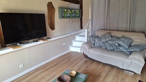 A living room with a flat-screen TV, a sofa with patterned cushions, a wooden bowl, and a staircase. - Charming French cottage/charming country house (Le Plessis-Dorin)