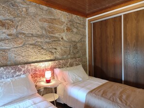 Quarto com parede de pedra, teto de madeira e cama com roupa de cama branca.