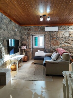 Uma sala de estar aconchegante com parede de pedra, televisão de tela plana, sofá e janela com persianas.