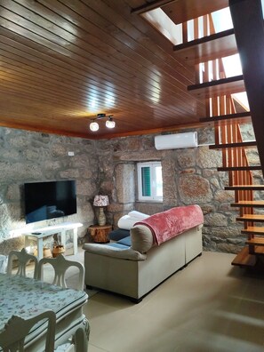 A cozy living room with a stone wall, a flat-screen TV, a wooden ceiling, and a staircase. - Oak House - A Retreat in Caramulo (São João do Monte - Vale do Lobo)