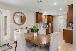A dining area with a wooden table and chairs, a potted plant, and a kitchen in the background. - Scottsdale Montecito Retreat | Pool, Hot Tub, Putting Green & Games 🌵⛳ (Scottsdale)