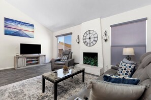A modern living room with a flat-screen TV, a fireplace, and a large clock on the wall. - Scottsdale Old Town Basecamp | Single-Level 3BR, Pool Access & Golf 🌵⛳ (Scottsdale)