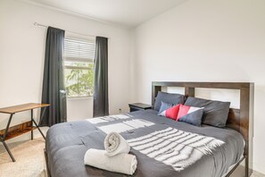 Ein ordentlich bezogenes Bett mit einer grauen Daunendecke, Kissen und einem aufgerollten weißen Handtuch.