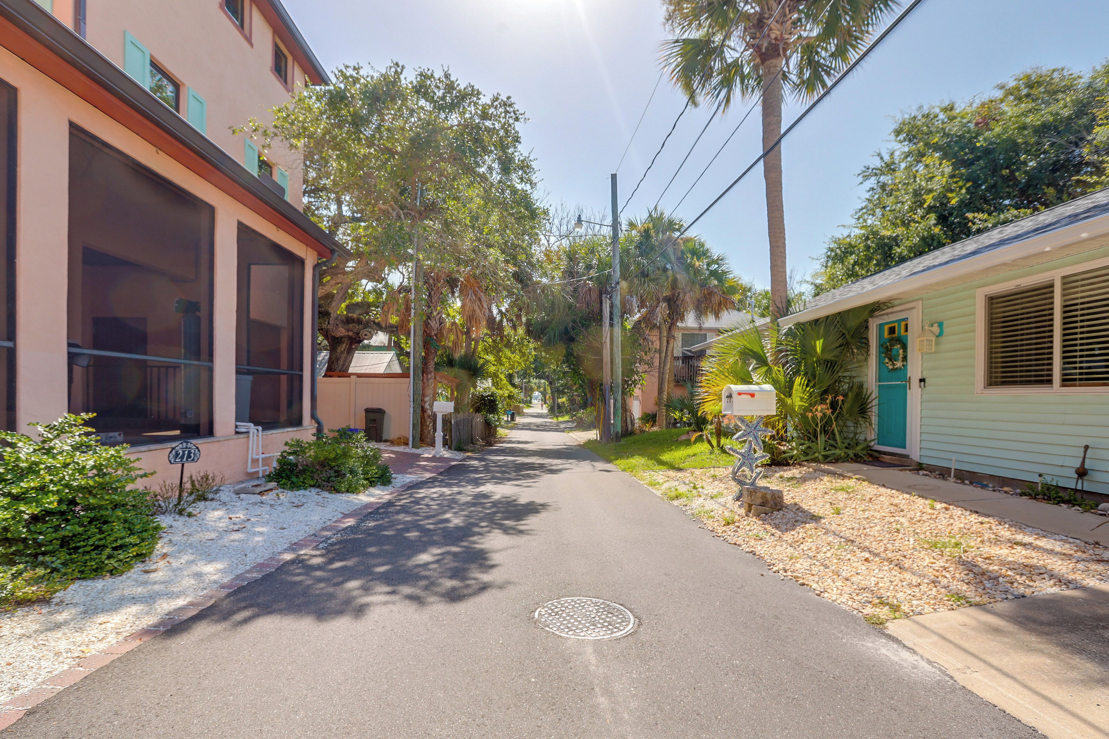 Rua residencial com casas em ambos os lados, céu claro e uma tampa de bueiro no meio da estrada.