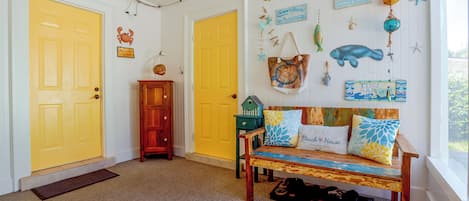 A room with two yellow doors, a wooden bench with beach-themed cushions, and various nautical decorations on the walls.