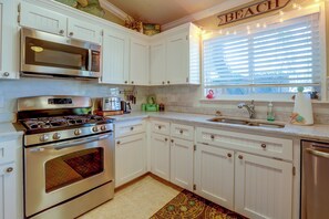 A kitchen with white cabinets, stainless steel appliances, a window with blinds, and a decorative flamingo.