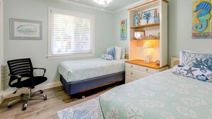 A bedroom with a bed, a desk, a chair, a ceiling fan, and artwork on the walls. - Flip-flop to Beach & Flagler Ave! Breezy Getaway (New Smyrna Beach)