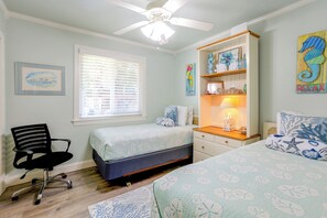 Ein Schlafzimmer mit einem Bett, einem Schreibtisch, einem Sessel, einem Deckenventilator und Kunstwerken an den Wänden.