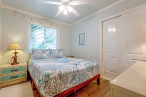 A bedroom with a bed, a nightstand, a lamp, a window with blinds, a ceiling fan, and a door. - Freshly Updated, Flip-flop 2 Blocks to Beach! (New Smyrna Beach)