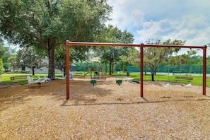 A playground with swings, a slide, and a climbing structure. - Heated Pool & Game Room! Family Hub 9 Mi to Disney (Davenport)