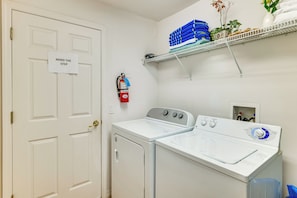 A laundry room with two white washers and dryers, a fire extinguisher, and a shelf with folded towels and plants. - Heated Pool & Game Room! Family Hub 9 Mi to Disney (Davenport)
