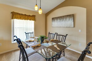 A dining area with a glass table, six chairs, a potted plant, and a painting on the wall. - Heated Pool & Game Room! Family Hub 9 Mi to Disney (Davenport)