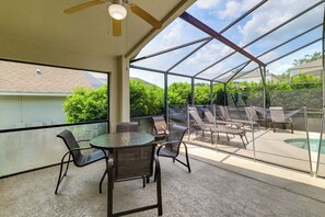 A covered patio area with a table and chairs, a ceiling fan, and a view of a swimming pool through a glass enclosure. - Heated Pool & Game Room! Family Hub 9 Mi to Disney (Davenport)