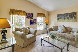 A living room with two sofas, a coffee table, and two lamps. There are two windows with curtains, and artwork on the walls. - Heated Pool & Game Room! Family Hub 9 Mi to Disney (Davenport)