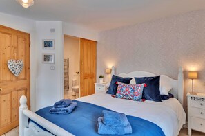 A bedroom with a bed, two bedside tables, a nightstand, a wooden wardrobe, and a bathroom visible through an open door. - Chester House (Dolgellau)