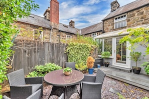 A patio area with a round table and chairs, surrounded by plants and a wooden fence. - Chester House (Dolgellau)