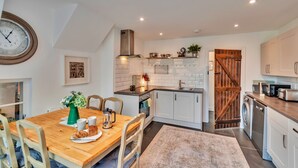 Una cocina moderna con armarios blancos, una mesa de comedor de madera y un reloj en la pared.