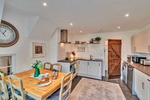 Eine moderne Küche mit weißen Schränken, einem Holztisch und einer Uhr an der Wand.