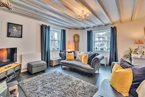 A living room with a sofa, ottoman, and a television. - Chester House (Dolgellau)