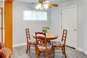 Un coin repas avec une table et des chaises en bois, un ventilateur de plafond et une fenêtre avec des stores.