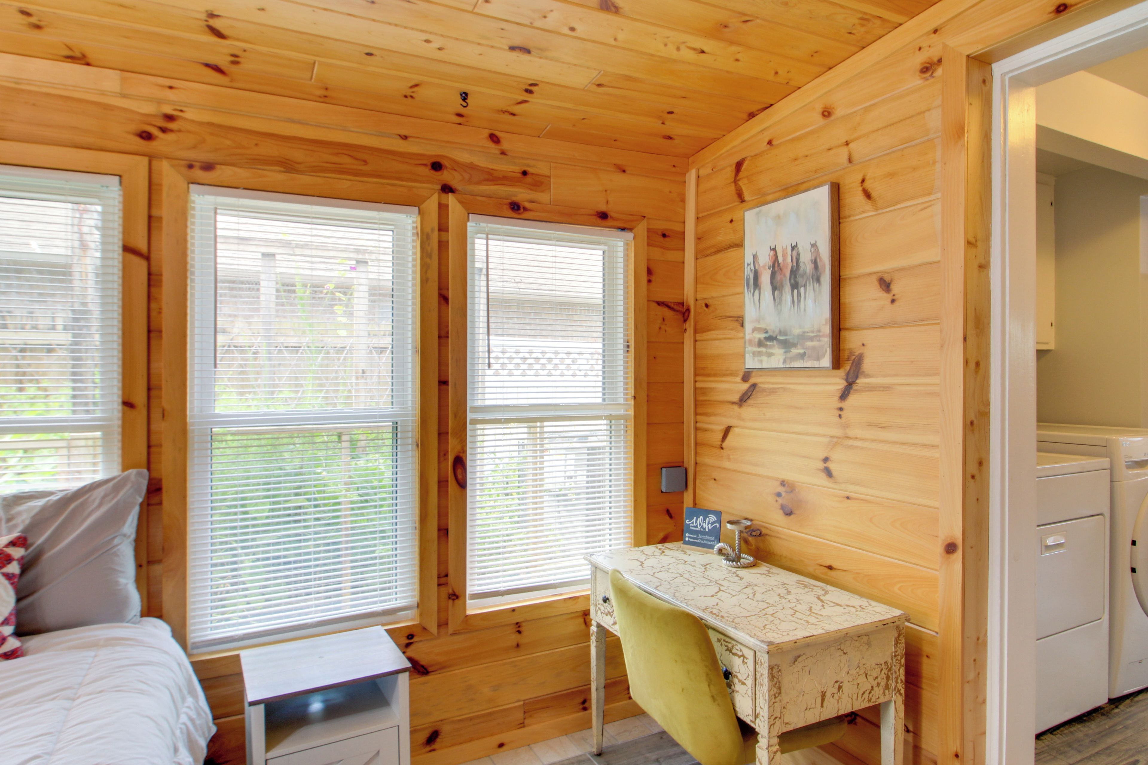 A room with wooden walls, a bed, a desk, and a washing machine.