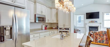 Une cuisine moderne avec des meubles blancs, des appareils en acier inoxydable, un îlot central et un lustre.