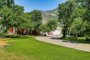 Ein Auffahrt, die zu einem Haus mit Garage führt, umgeben von üppigen, grünen Bäumen und einer hügeligen Landschaft im Hintergrund.