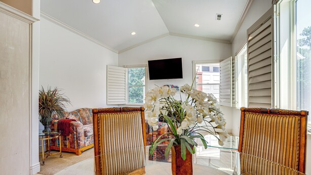A spacious living room with a large window, a flat-screen TV mounted on the wall, and a central table with a vase of flowers. - Full Kitchen! King Suite Near Snowbasin (Layton)