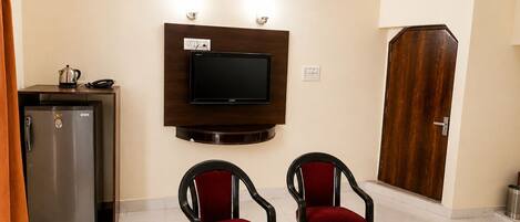 A hotel room with a wooden table, two chairs, a television mounted on the wall, a minibar, and a door.
