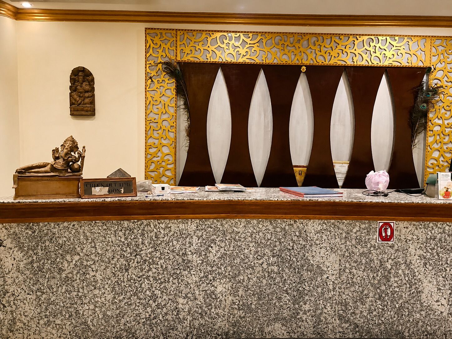 A reception desk with a decorative panel, a statue, and a sign indicating the check-out time.