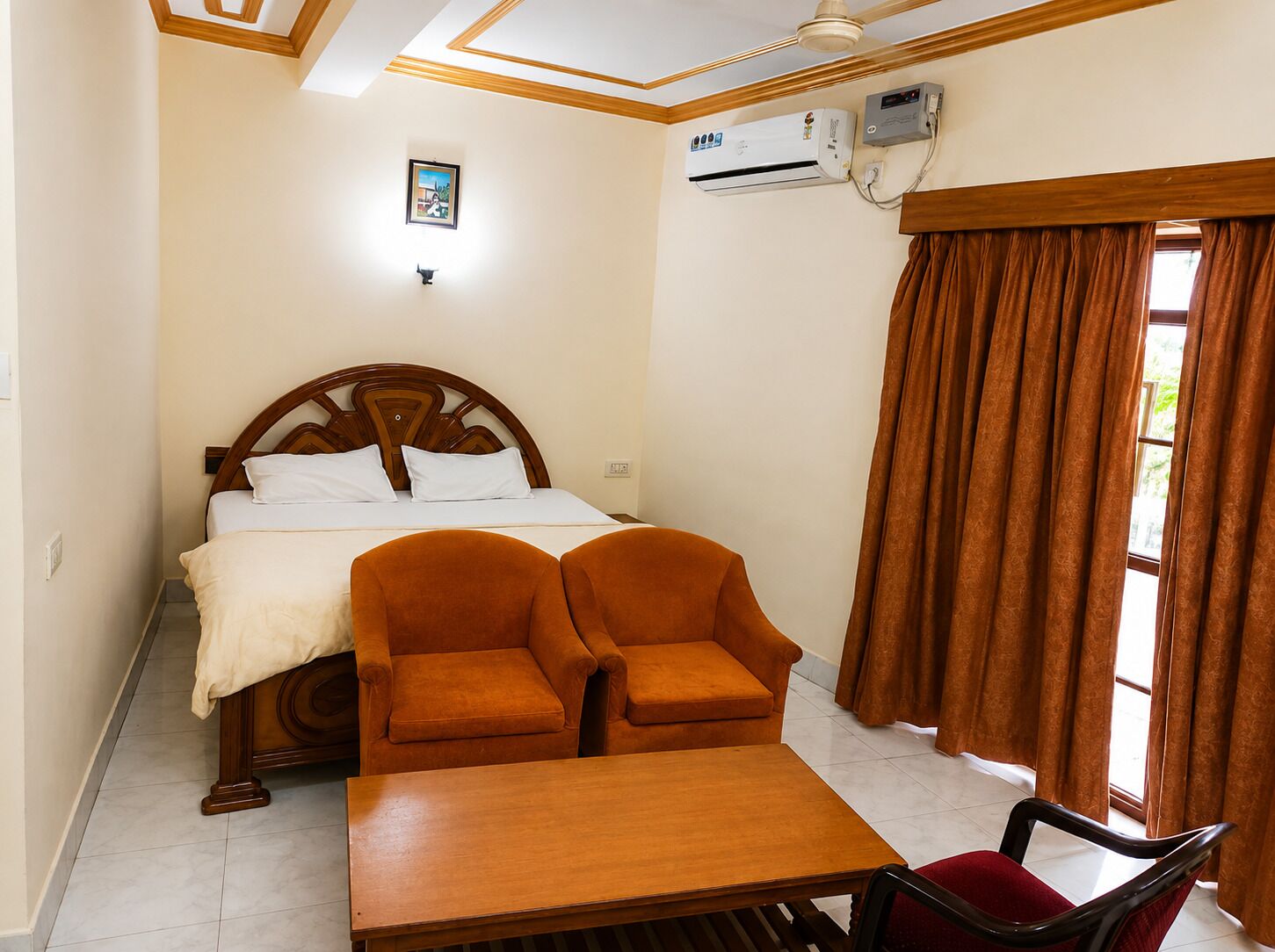 Habitació d'hotel amb un llit, dos seients, una taula, aire condicionat i una finestra amb cortines.