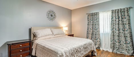 A bedroom with a bed, nightstand, dresser, ceiling fan, and patterned curtains.