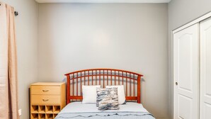 A bedroom with a wooden bed frame, a bedside table, a wardrobe, and a wall-mounted light fixture. - Walk to Tucson Trails! Private Yard w/ Views (Tucson)