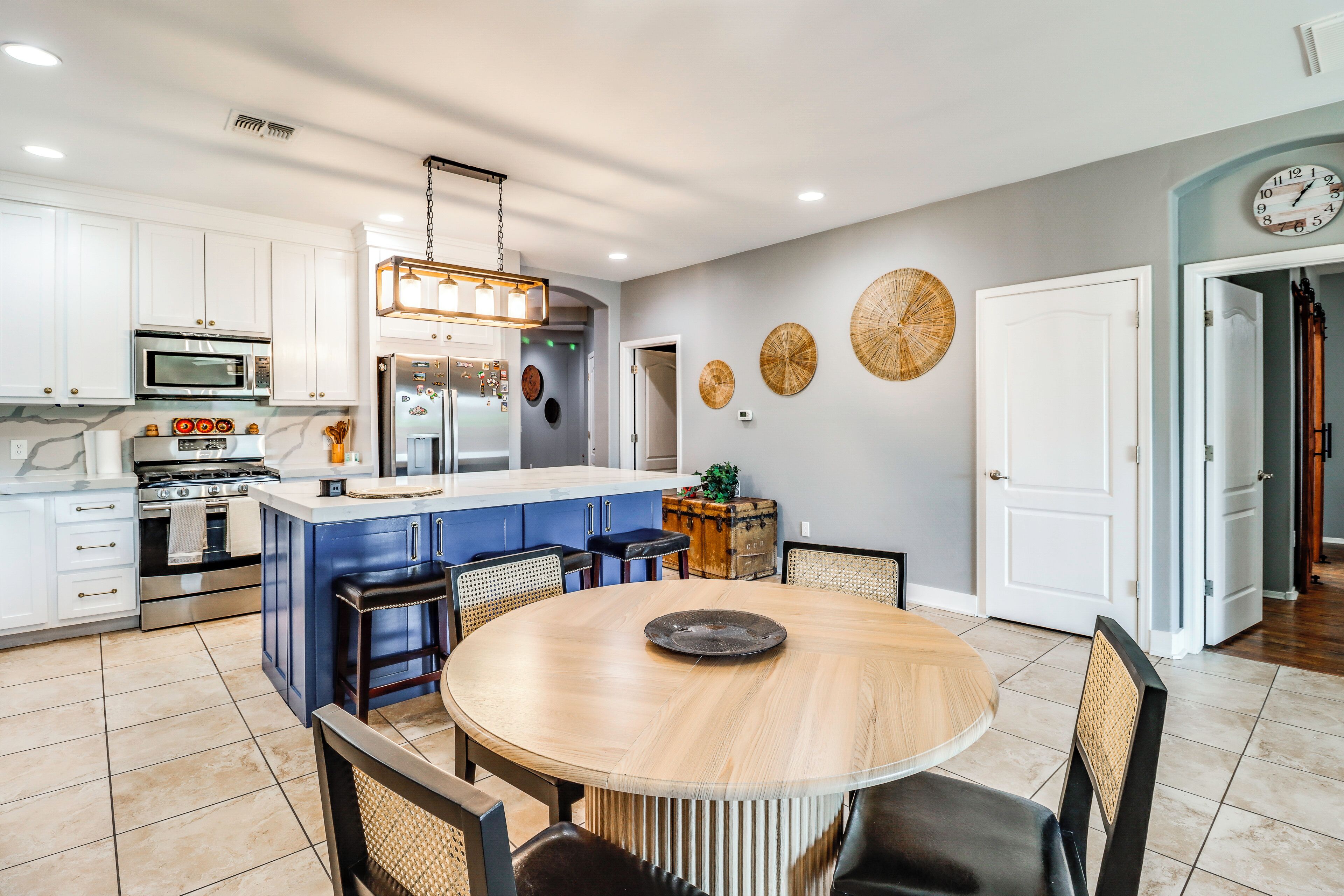 A modern kitchen with white cabinets, a central island, and a dining area with a round table and chairs.
