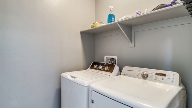 A laundry area with a front-loading washer and dryer, a shelf with cleaning supplies, and a wall-mounted control panel. - Walk to Tucson Trails! Private Yard w/ Views (Tucson)