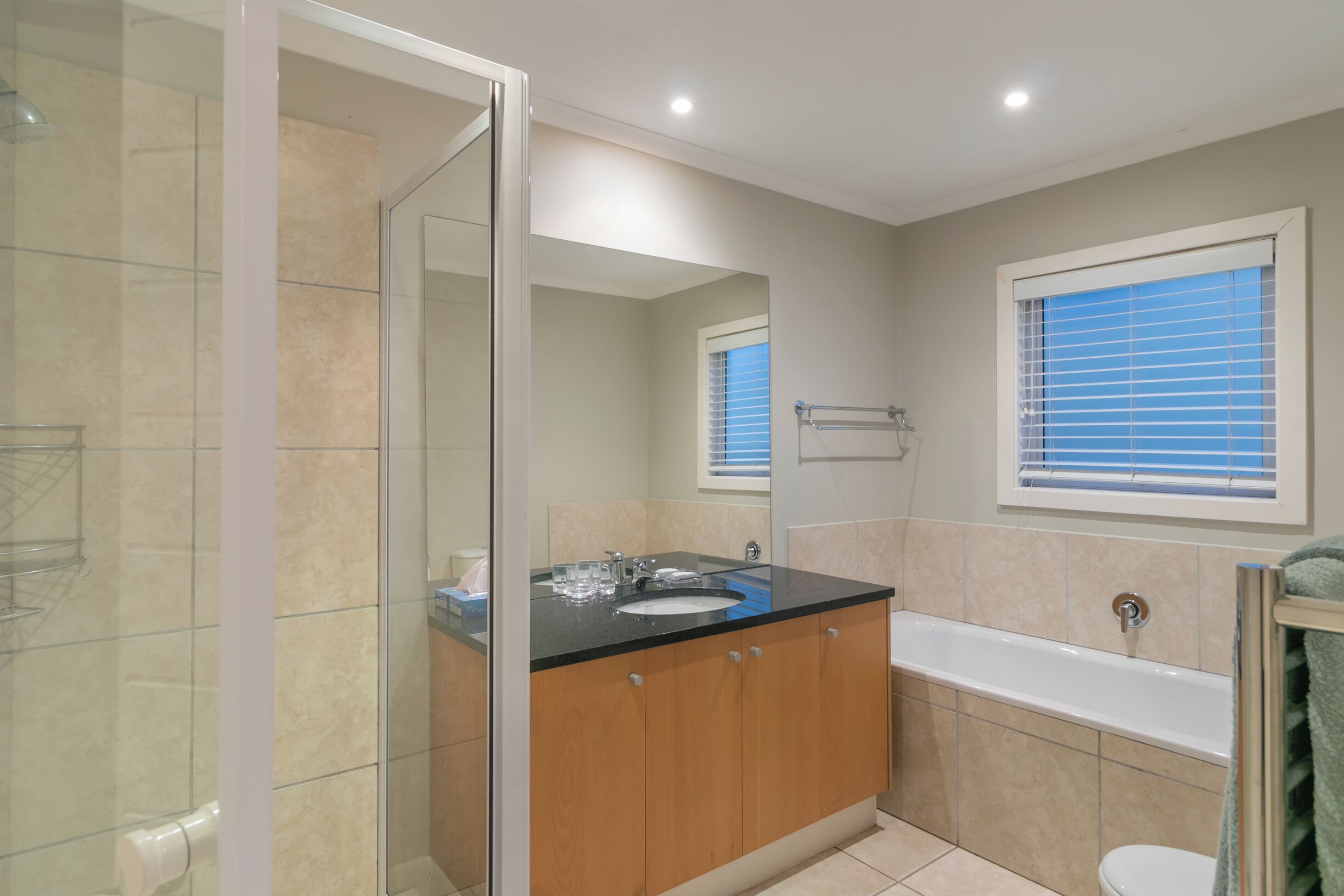 A modern bathroom with a glass shower enclosure, a vanity with a black countertop, a white sink, and a bathtub.