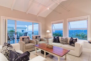 A spacious living room with a large sliding glass door leading to an outdoor patio, a wooden coffee table, and a sofa with patterned cushions. - Afternoon Delight NT3 (Knysna)