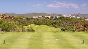 Un campo de golf con cielo despejado, un césped cuidado y una vista distante de edificios residenciales.