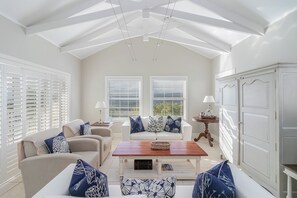 A bright, white interior with a high ceiling, two windows with blinds, a white sofa set, and a wooden coffee table. - Afternoon Delight NT3 (Knysna)