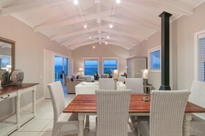 A spacious living area with a high ceiling, a dining table, wicker chairs, and a view of the city through large windows. - Afternoon Delight NT3 (Knysna)