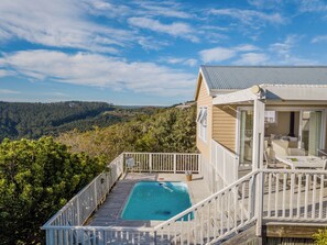 A pool on a wooden deck with a view of a forested hillside.