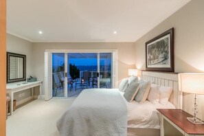 Une chambre dotée d’un grand lit, d’un bureau, d’une chaise, d’un balcon avec vue et d’un tableau encadré au mur.