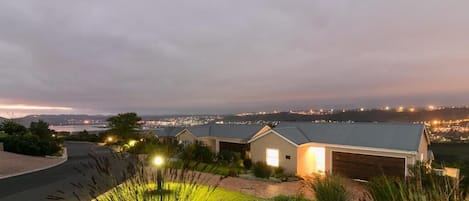 A residential area with houses, a driveway, and a view of a distant cityscape at dusk.