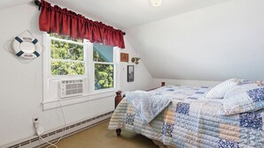 A bedroom with a bed, a window with a red valance, a life preserver decoration, and a ceiling light. - Lakefront Paradise on Lake Wallenpaupack w/ Dock (Hawley)