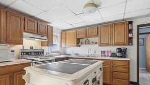 A kitchen with wooden cabinets, a stove, a microwave, and a coffee maker. - Lakefront Paradise on Lake Wallenpaupack w/ Dock (Hawley)